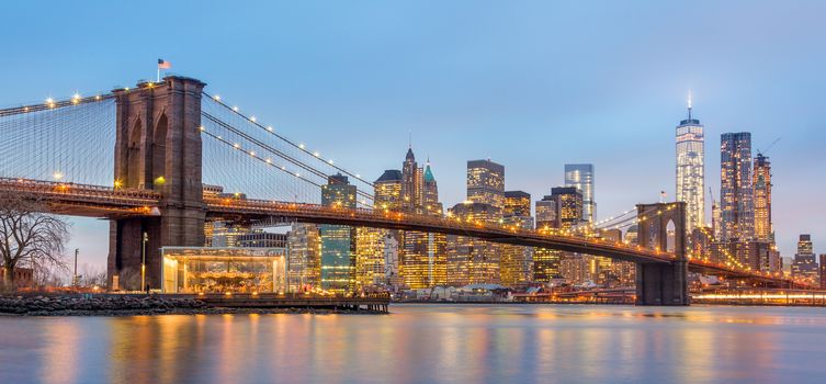 Brooklyn bridge and New York City Manhattan downtown skyline at dusk with skyscrapers illuminated over East River panorama. Panoramic composition.