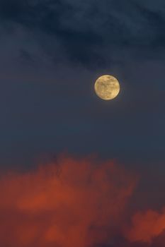 Moonrise in the East during sunset with pink clouds and blue sky