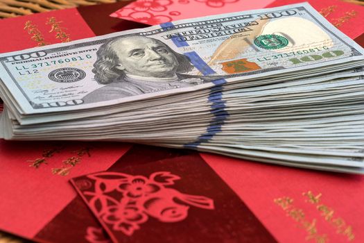 Stack of USD One Hundred Dollars notes on top red packets with Chinese text wishing Wealth and Happiness for Chinese Lunar New Year