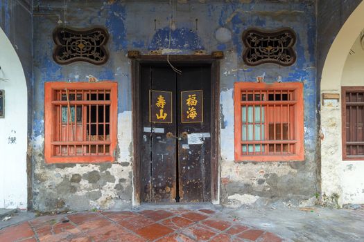 Old Run-Down Peranakan style home exterior with Chinese text Longevity Mountain and Properous Sea on wooden doors entrance