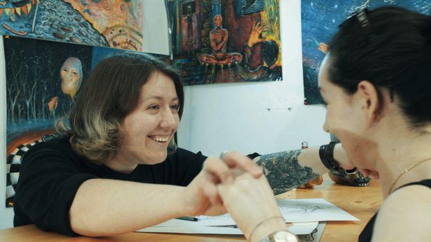 Portrait of two womans in tattoo salon. They are glad to see each other. Medium shot