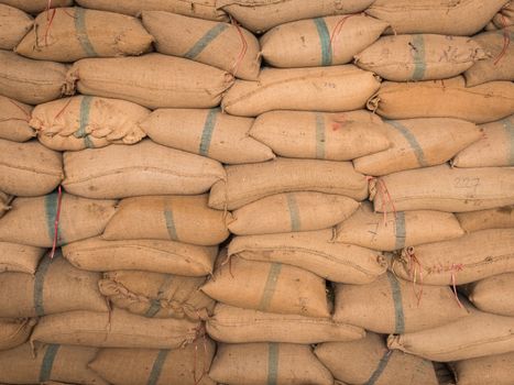 Old hemp sacks containing rice placed stacked in a row.