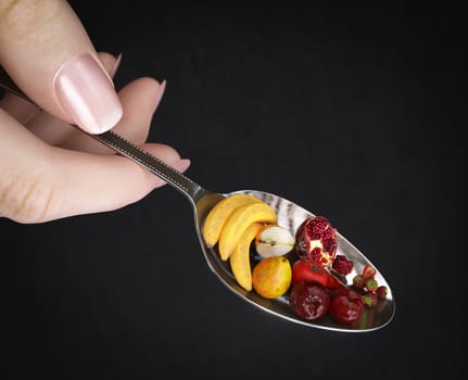 woman hand holding spoon with fruits on isolate black diet concept photo closeup