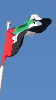 A huge flag of United Arab Emirates - UAE  fluttering in the wind, against clear blue skies.