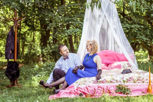 Man and woman sitting on the bed in the lawn and man takes off shoes from women in Lviv, Ukraine.