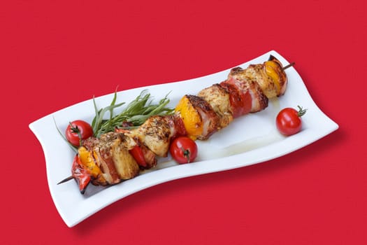 Skewers of meat and vegetables on the grill, with tomatoes and fresh herbs, on a red tablecloth