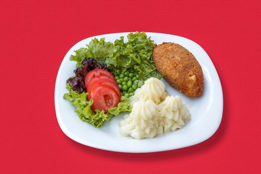 Mashed potatoes with a cutlet, vegetable, tomato and green peas on a red tablecloth