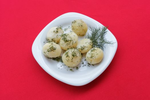 Boiled potatoes with herbs on a plate and red tablecloth. Close-up view from above.