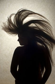 A silhouette of a young woman flipping her long hair