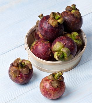 Arrangement of Fresh Ripe Mangosteen in Wooden Bowl closeup on Light Blue Wooden background