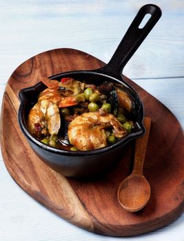 Delicious Seafood Curry with Prawns, White Fish, Mussels and Vegetables in Black Iron Cast Pot with Wooden Spoon closeup on Serving Board