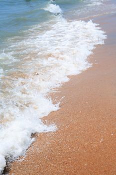 Closeup of sea wave with foam on beach sand. Vacation background