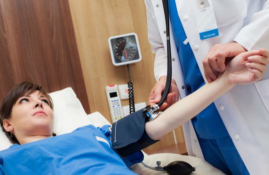 A doctor is measuring the blood pressure of a young beautiful patient on a bed in hospital.