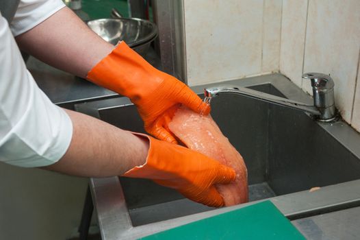 Hands in gloves washing and cleaning salmon fish at the kitchen sink