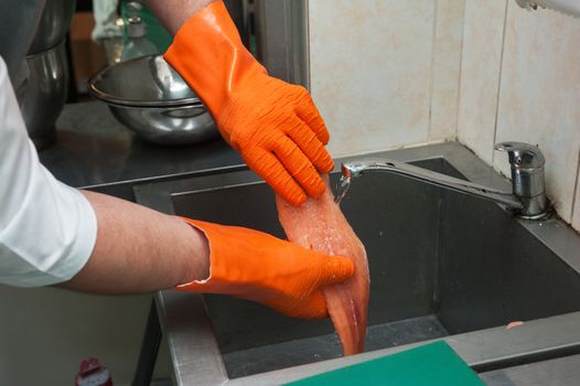 Hands in gloves washing and cleaning salmon fish at the kitchen sink