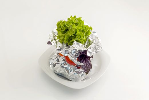 Meat, vegetables, fish baked in aluminum foil and decorated with fresh herbs. On a white plate close-up