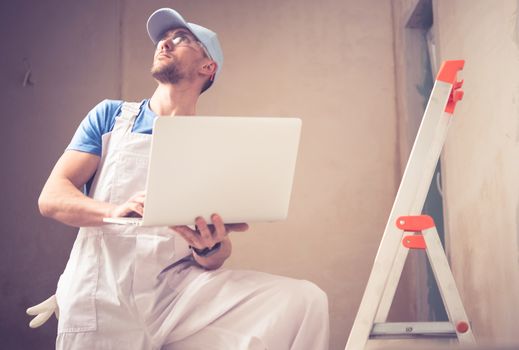 Caucasian Construction Worker with Laptop Managing Remodeling Project. 