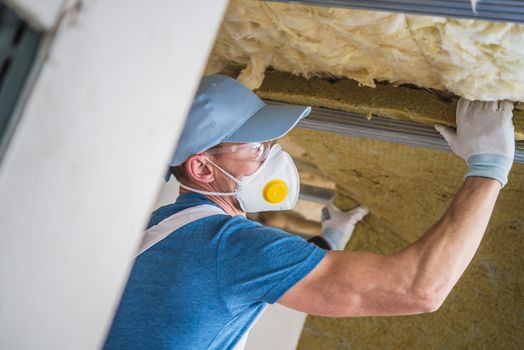 Mineral Wool Insulation by Professional Insulating Worker. Caucasian Construction Worker in His 30s.