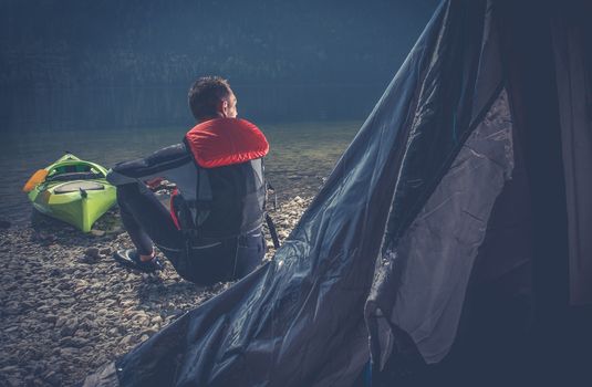 Outdoor Sportsman Camping. Caucasian Men in Wetsuit on the Camping on the Edge of Scenic Lake.