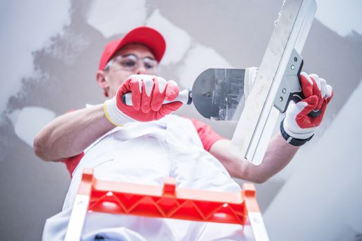 Professional Caucasian Construction and Remodeling Worker Preparing For Drywall Patching  Mixing Joint Compound While Staying on the Ladder.