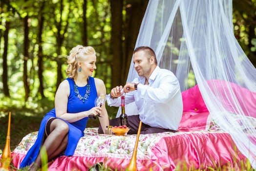 Man and woman sitting on the bed in the lawn and opening wine bottle in Lviv, Ukraine.