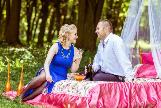 Man and woman sitting on the bed in the lawn with an open bottle of wine and a glass in Lviv, Ukraine.