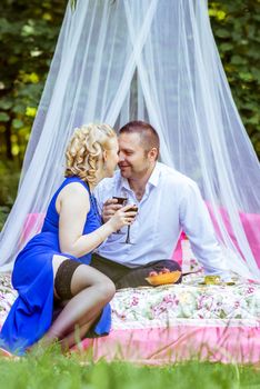Man and woman sitting on the bed in the lawn and holding a glasses of wine and look at each other in Lviv, Ukraine.