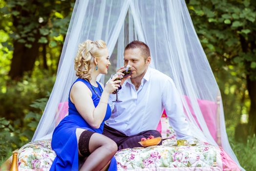 Man and woman sitting on the bed in the lawn and drinking wine from glass and look at each other in Lviv, Ukraine.