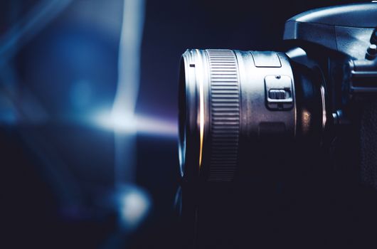 Digital Camera and the Photography Concept Photo. Dark Blue Color Grading with Little of Light. Camera Side View.