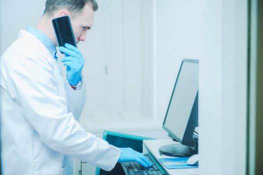 Doctor Consulting Results of Patient Testing While Staying in the Room in Front of His Office Computer and Talking by Phone. Caucasian Doctor.