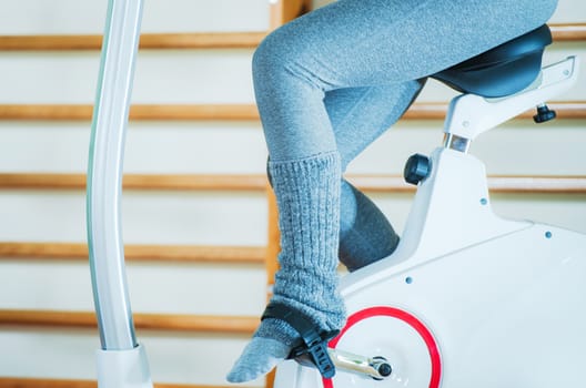Girl on Exercise Bike in the Fitness Center. Pedaling Legs Closeup Photo.