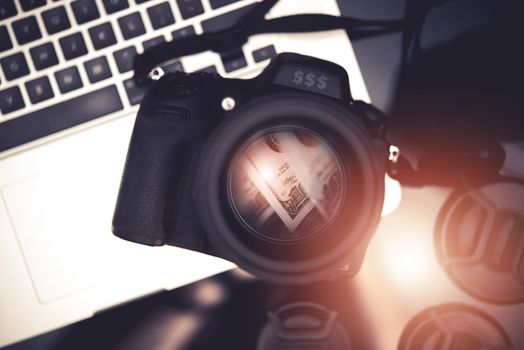 Microstock Photo Business Concept Photo with Digital Camera and Dollar Banknotes Reflection Inside the Lens and Laptop Computer. Making Money Taking Pictures.