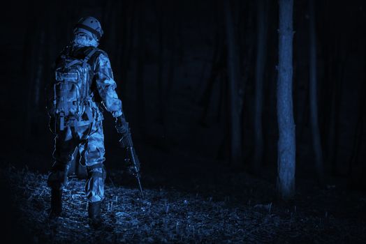 Military Operation at Night. Dark Blue Color Grading Concept. Soldier with the Rifle Staying Back in the Middle of the Pitch Dark Forest.