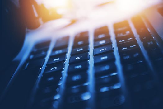 Modern Laptop Computer Workstation Closeup Photo. Computer and Digital Technology Concept Photo. Dark Blue Gradient with Reddish Light Source.