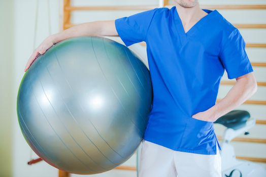 Caucasian Male Rehabilitation Specialist with Ball Awaiting Next Patient. Rehabilitation Center.