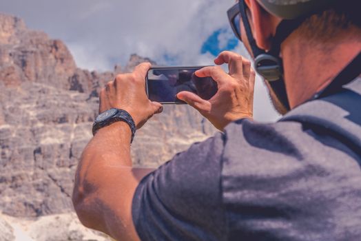 Taking Photos Using Smartphone Device. Caucasian Biker in Bike Helmet Taking Picture of the Scenic Mountain Place.