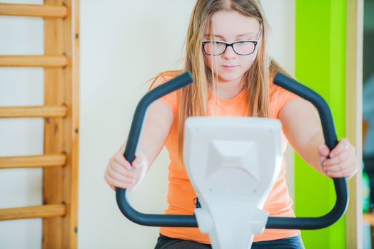 Teenage Girl on Exercise Bike in the Fitness Center. Closeup Photo.