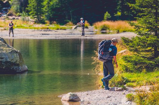 Traveling Adventurous Men on the Edge of Scenic Mountain Lake. Caucasian Traveler with Large Backpack on the Mountain Trail.