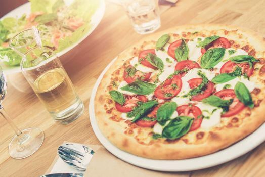 Tasteful Tomato Basil Pizza on the Wooden Restaurant Table.