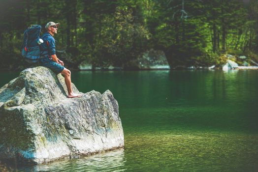 Traveling Men Taking Break on a Rock on the Edge of Scenic Mountain Lake. Caucasian Hiker on the Trail.