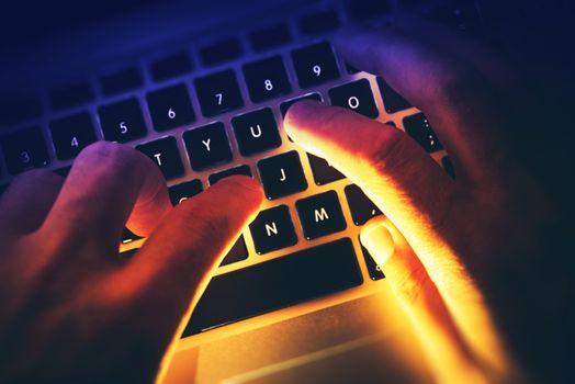 Typing on the Computer by Hacker or Programmer Concept Photo. Hands on Laptop Computer Keyboard with Strong Bright Light Coming From Back.