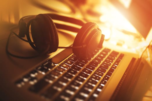 Listening Music While Working. Laptop Computer and Modern Headphones Closeup Photo. Reddish Warm Colors.