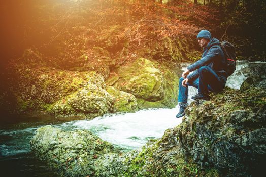 Young Caucasian Hiker on the Mountain Trail Resting on the Large Mountain River Boulder.