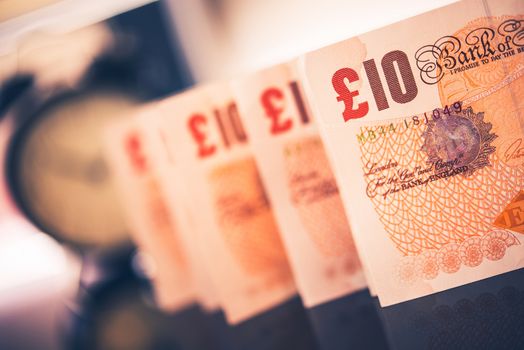British Pounds in a Row on the Glassy Table. Classic Clock in the Background.
