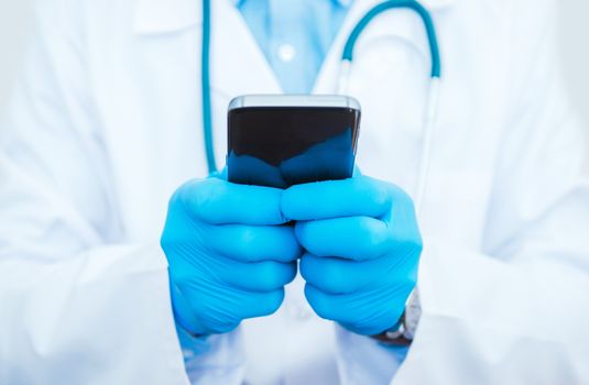 Doctor Playing Smartphone. Medical Doctor in Blue Medical Glove Browsing Data on His Mobile Phone Using Medical Mobile Applications.