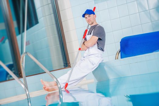 Swimming Pool Technician Cleaner Taking Rest Break On the Edge of Large Indoor Pool.