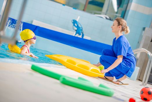 Swimming Pool Rehabilitation For Children. Female Caucasian Physician Playing with Disabled Girl on the Swimming Pool.