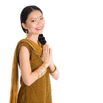 Young mixed race Indian Chinese girl in traditional punjabi dress greeting gesture, standing isolated on white background.