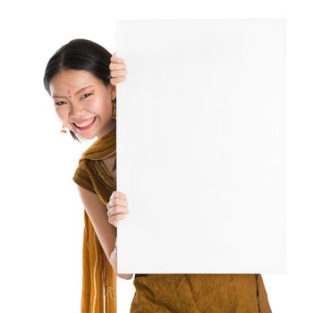 Portrait of young mixed race Indian Chinese girl in traditional punjabi dress hiding behind a blank white paper card, standing isolated on white background.