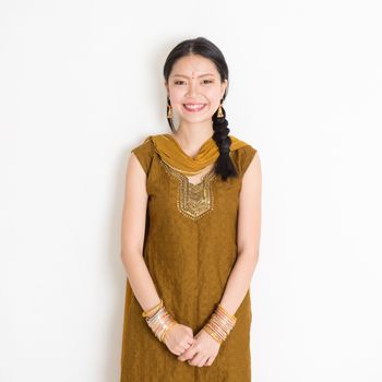 Portrait of young mixed race Indian Chinese woman in traditional Punjabi dress smiling, standing on plain white background.